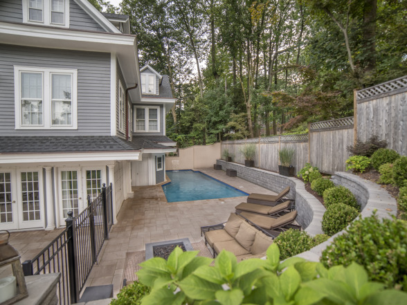 Inground pool beside a gray-shingled home with stone accent siding