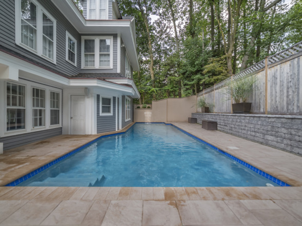 After photo of a backyard pool installation with gray-sided home and landscaping