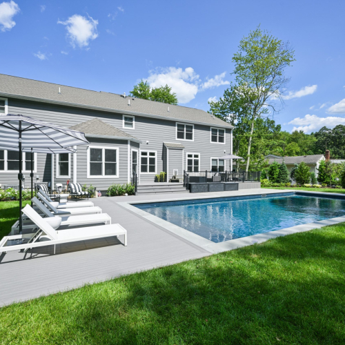 Modern backyard pool with lounge chairs and umbrella, surrounded by lush greenery, showcasing a completed project by EverClear Pools & Spas in Berkley Heights, NJ.