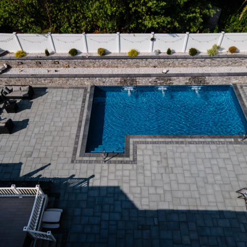 Aerial view of a modern in-ground pool surrounded by a spacious patio, featuring lounge seating and decorative landscaping, showcasing a completed pool project by EverClear Pools & Spas in Clifton, NJ.