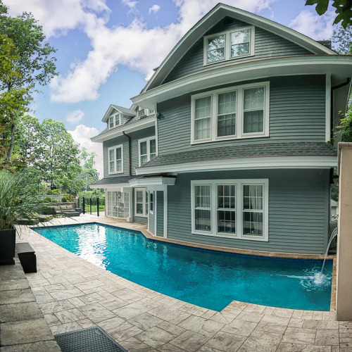 Poolside view of an inground pool adjacent to a green Victorian-style home