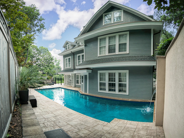 Poolside view of an inground pool adjacent to a green Victorian-style home