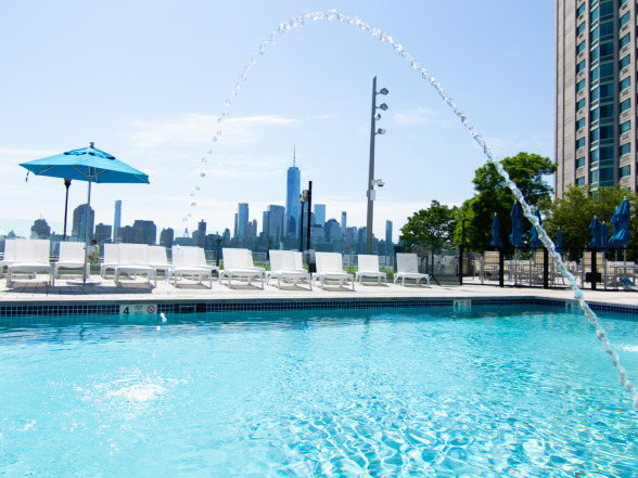 Daytime overhead angle of the commercial pool with rows of lounge chairs and blue patio umbrellas