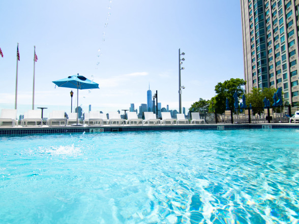 Wide view of the commercial gunite pool with Blue Quartz plaster, paver pool deck, and high-rise buildings in the background