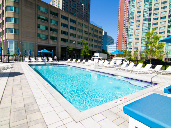 Corner view of the commercial pool showing the integrated spa, paver decking, and urban skyline