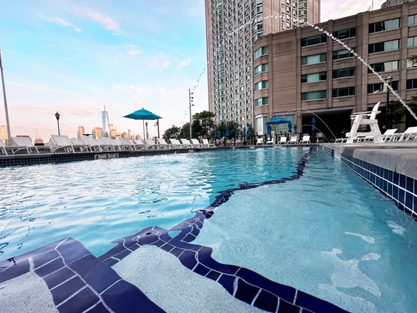 Twilight view of commercial gunite pool with lounge chairs and Manhattan skyline backdrop