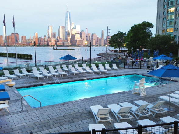 Daytime overhead angle of the commercial pool with rows of lounge chairs and blue patio umbrellas