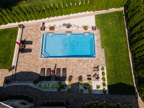 Aerial drone view of the full backyard showing the rectangular pool, stone paver patio, fire bowls, and arborvitae hedge