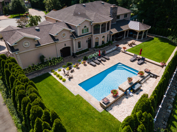 Aerial view of a rectangular pool with paver patio, outdoor pavilion, lounge seating, and arborvitae privacy hedge