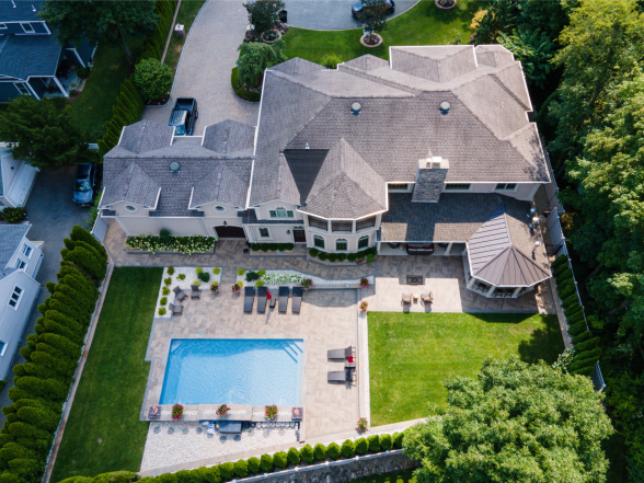 High-altitude drone shot of the property showing pool, paver patio, and estate-style home with turret roof