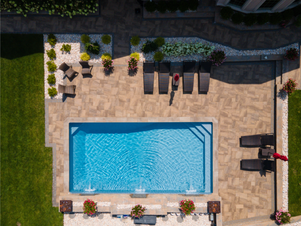 Overhead view of a rectangular pool with red patio umbrellas, lounge chairs, and stone paver surround