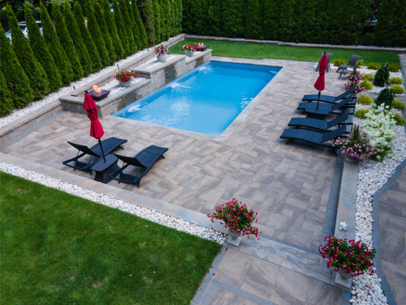 End-on view of the pool highlighting the natural stone paver pattern, raised water feature, and mature evergreen screening
