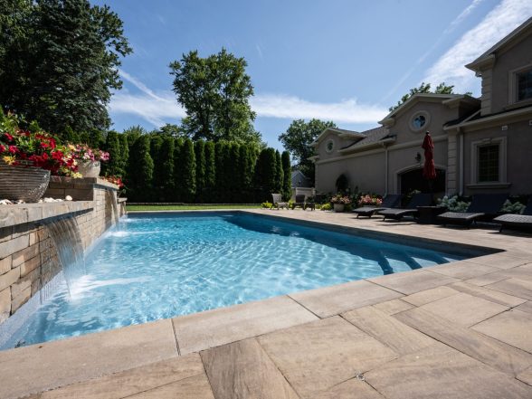 Angled view of the pool from the deep end with natural stone paver coping and arborvitae privacy wall