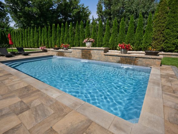 Angled view of the pool from the deep end with natural stone paver coping and arborvitae privacy wall