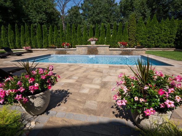 Pool corner detail showing natural stone paver patio, rose garden plantings, and fire bowl on stone pillar