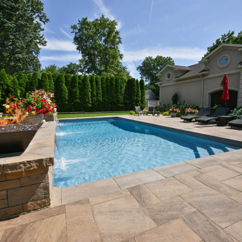 Luxury backyard featuring a sparkling in-ground pool, elegant stone coping, vibrant flower arrangements, and a fire feature, showcasing a completed pool project by EverClear Pools & Spas.