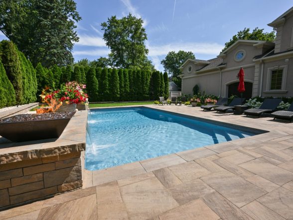Luxury backyard featuring a sparkling in-ground pool, elegant stone coping, vibrant flower arrangements, and a fire feature, showcasing a completed pool project by EverClear Pools & Spas.
