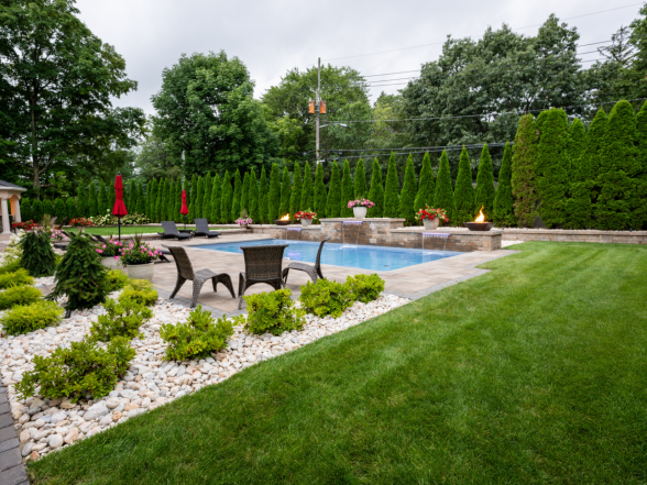 Rear view of the pool and patio with outdoor dining area, white rock border, and arborvitae privacy hedge