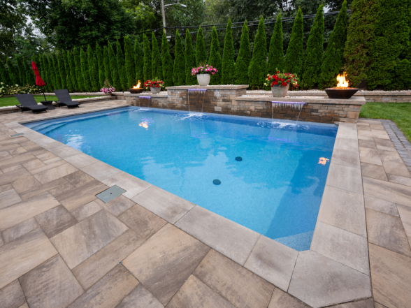 Corner angle of the rectangular pool showing stone water feature wall, fire bowls, and natural stone paver coping