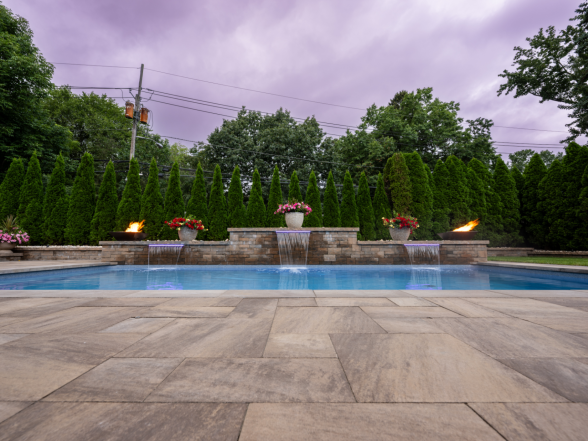 Twilight view of the pool with fire bowls lit, sheer descent water features flowing, and dramatic cloud sky