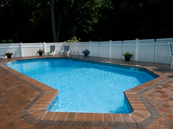 Freeform pool showing the full custom shape with herringbone-pattern brick paver border and Toffee Onyx coping