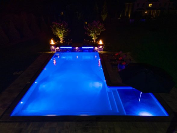 Nighttime view of the pool glowing blue with sheer descent waterfalls actively flowing from raised stone pillars