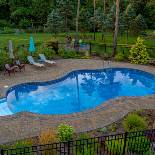 Custom in-ground pool surrounded by a stone patio, lounge chairs, and lush landscaping in Long Valley, NJ, showcasing EverClear Pools & Spas pool design and construction services.