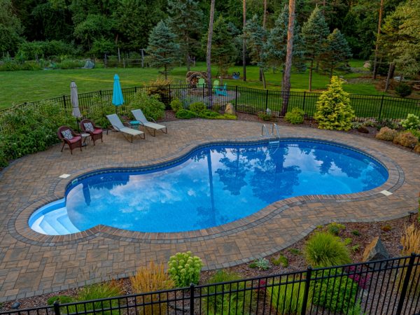 Custom in-ground pool surrounded by a stone patio, lounge chairs, and lush landscaping in Long Valley, NJ, showcasing EverClear Pools & Spas pool design and construction services.