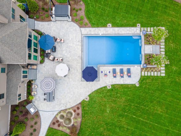 High-altitude aerial of the complete property showing the pool, paver patio, deck connection to the home, and landscaped yard