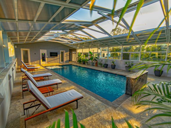Elevated view of the pool enclosure interior with Tahiti Blue water, travertine deck, and lush tropical plantings
