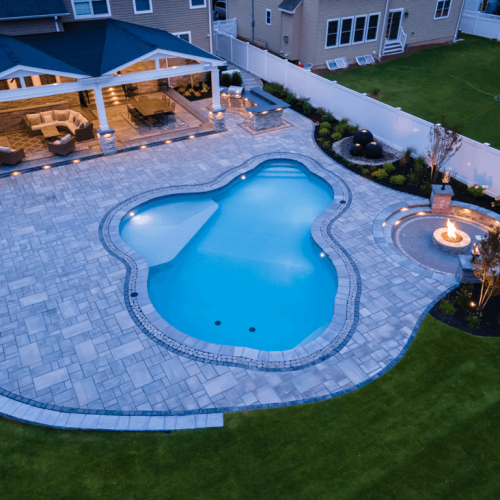 Aerial view of a custom-shaped swimming pool with a stone patio, surrounded by landscaped gardens and an outdoor seating area, showcasing a completed pool project by EverClear Pools & Spas in East Hanover, NJ.