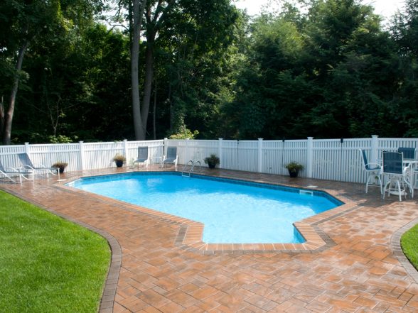 Freeform inground pool with brick paver patio, white vinyl semi-privacy fencing, and poolside lounge chairs at a completed project in Haskell, New Jersey