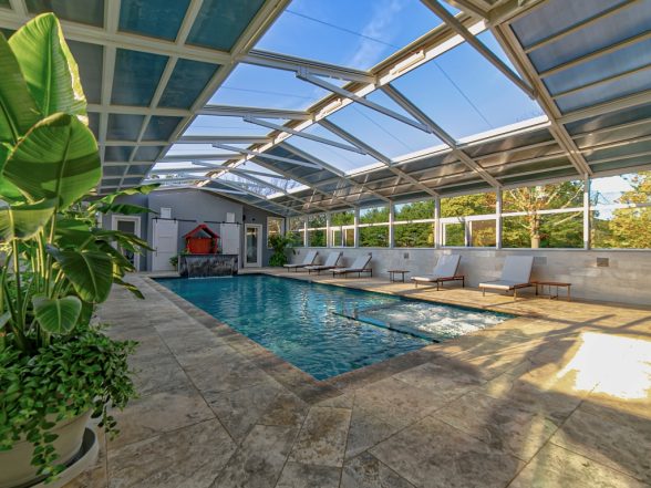 View from inside the enclosure looking toward the open end with travertine decking and tropical plants framing the pool