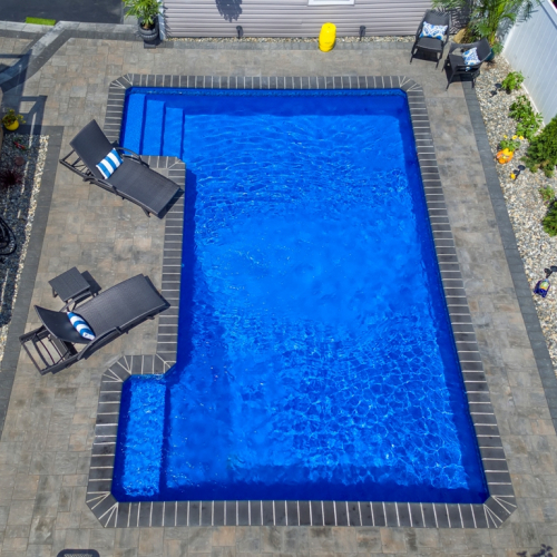 Gunite inground pool with vibrant blue water, surrounded by stone patio, lounge chairs, and landscaped area, showcasing a completed project by EverClear Pools & Spas in Lodi, NJ.