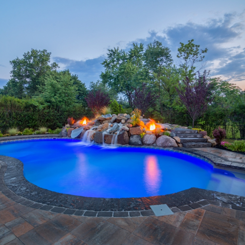 Gunite inground pool with vibrant blue water, surrounded by natural stone features, a waterfall, and landscaped greenery, showcasing a luxurious outdoor space by EverClear Pools & Spas.