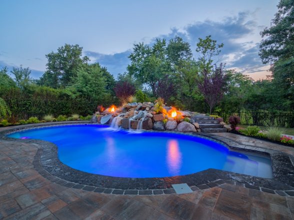 Gunite inground pool with vibrant blue water, surrounded by natural stone features, a waterfall, and landscaped greenery, showcasing a luxurious outdoor space by EverClear Pools & Spas.