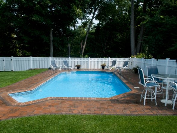 Corner perspective of the freeform pool with paver patio, white patio chairs, and white vinyl fencing