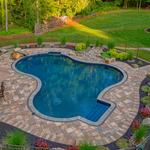 Gunite pool surrounded by a stone patio, landscaped with plants and rocks, featuring a shaded seating area, showcasing a completed project by EverClear Pools & Spas in Long Valley, NJ.