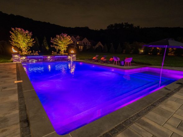 Nighttime purple-blue LED pool lighting with illuminated sheer descent water features and stone columns