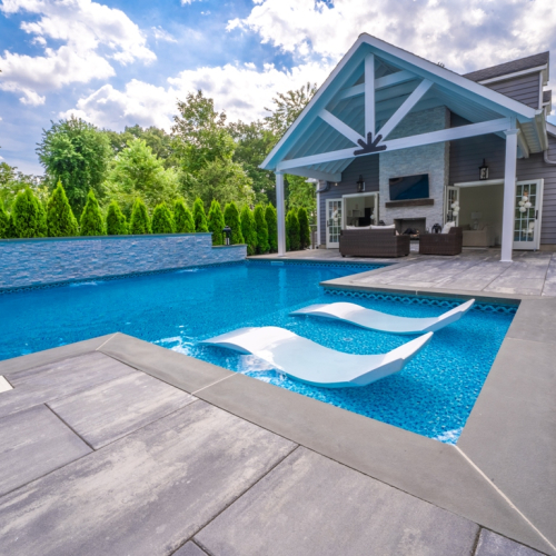 Modern pool design featuring a blue water pool with white lounge chairs, surrounded by lush greenery and a stylish outdoor living space, showcasing EverClear Pools & Spas construction expertise.