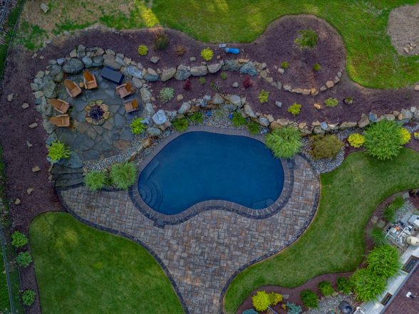 Aerial shot Gunite pool surrounded by a stone patio, landscaped with plants and rocks, featuring a shaded seating area, showcasing a completed project by EverClear Pools & Spas in Long Valley, NJ.
