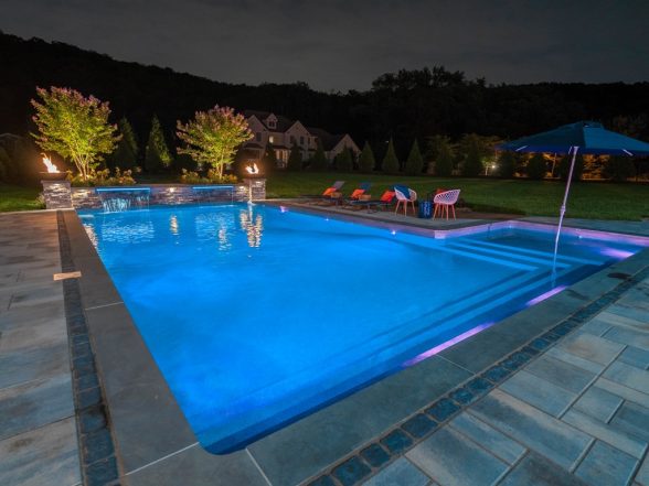 Pool lit with blue LED color-changing lights highlighting the sheer descent water features and bluestone coping