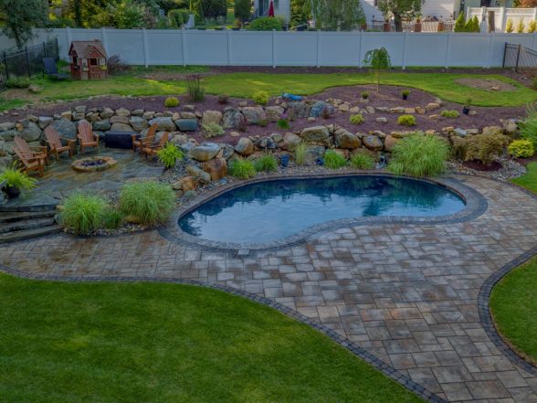 Side angle shot of a Gunite pool surrounded by a stone patio, landscaped with plants and rocks, featuring a shaded seating area, showcasing a completed project by EverClear Pools & Spas in Long Valley, NJ.