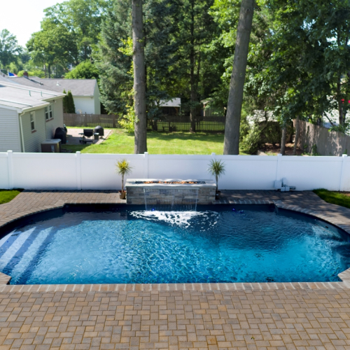 Vinyl pool installation with a waterfall feature, surrounded by a paved patio and lush greenery, showcasing a completed project by EverClear Pools & Spas in Clifton, NJ.