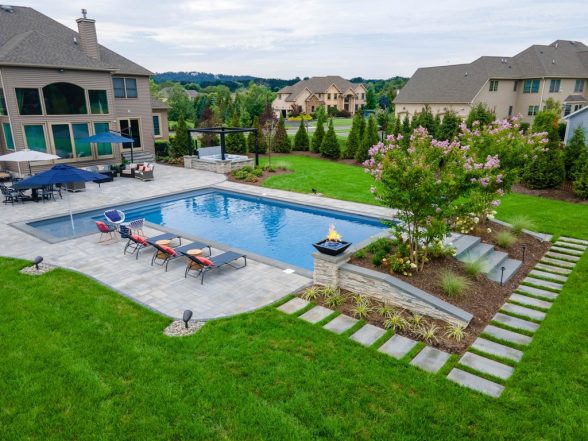 Wide-angle daytime view of the pool and yard with stepping stone pathway, raised stone pillars, and manicured lawn