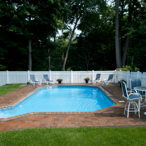 Vinyl pool surrounded by a white fence, featuring a brick patio, lounge chairs, and a table, showcasing a completed project by EverClear Pools & Spas in Haskell, NJ.