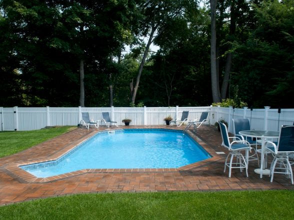 Vinyl pool surrounded by a white fence, featuring a brick patio, lounge chairs, and a table, showcasing a completed project by EverClear Pools & Spas in Haskell, NJ.
