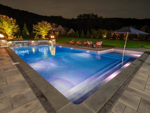 Nighttime view of the pool with raised stone sheer descent water features, fire bowls, and tanning ledge entry steps